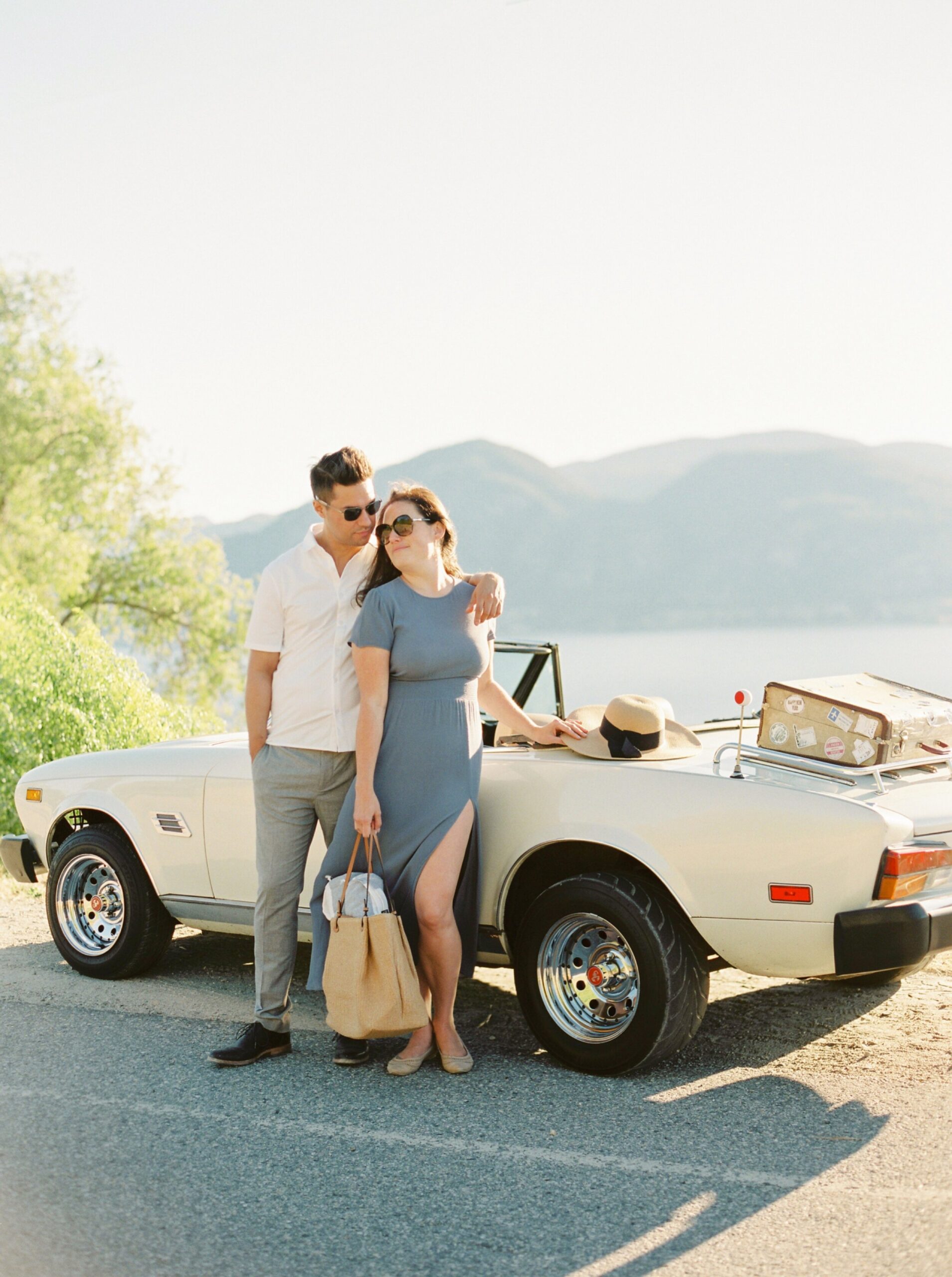 vintage white car and suitcase for a fun road trip in kelowna okanagan penticton vineyard on the naramata bench | summer engagement session | outfit ideas for couples photos | film photographer Jusitne Milton 