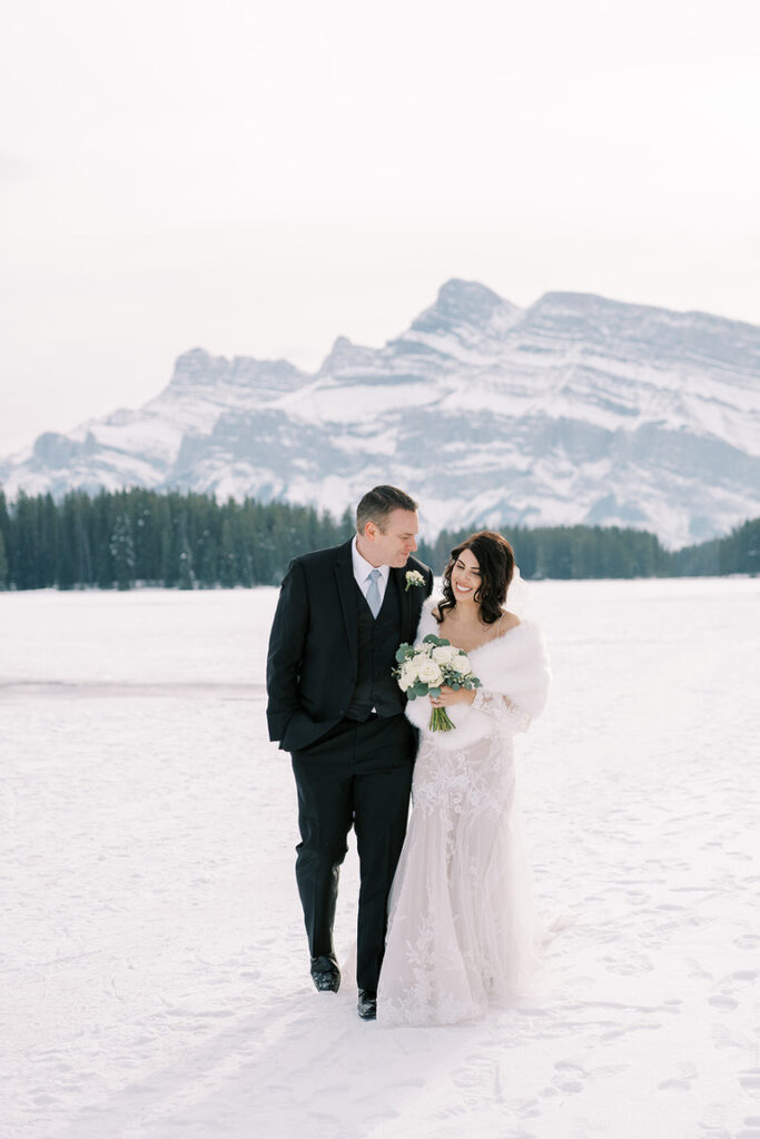 Bride and Groom wedding portrait shows couple kissing outside with winter mountains in the background,  Banff, Canada 