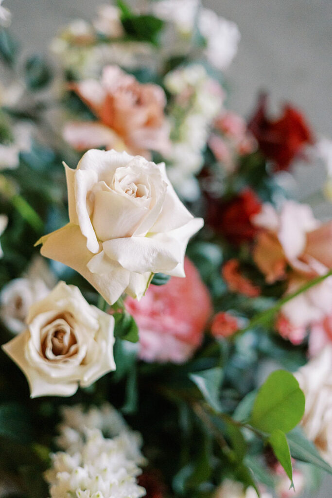 close up detail shot of wedding ceremony florals, soft pink roses are combined with reds, pinks, and green details. 