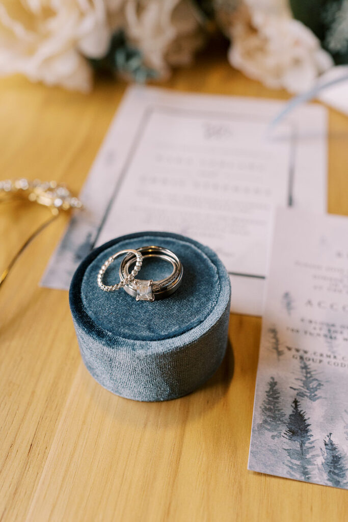 Close up photo of flat lay with wedding details including ring box with wedding ring, wedding bands and invitation. 