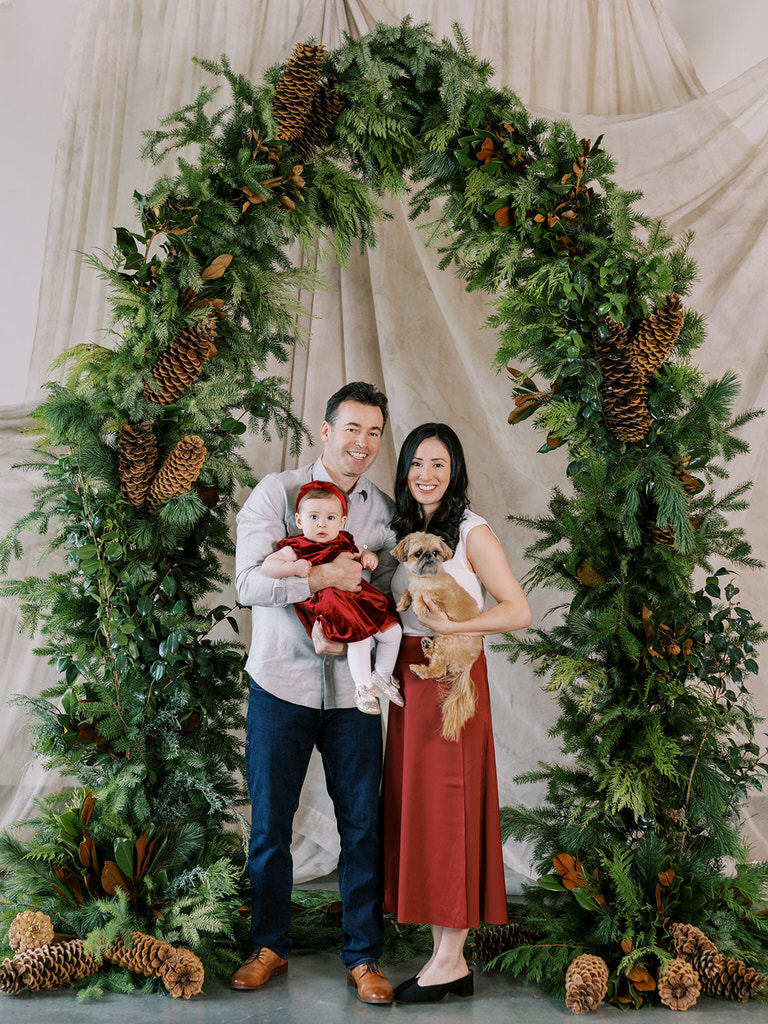 family christmas portrait under festive garland arch with fmaily dog and baby 