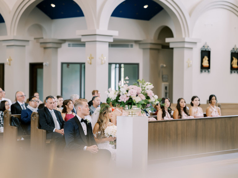 bride and groom at wedding ceremony, seated in pews of catholic church during readings