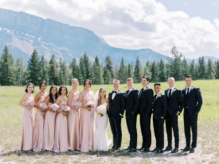 wedding party portraits in Canadian Rockies. Bride and Groom with groomsmen and bridesmaids. Pink satin dresses with pink and white roses. 