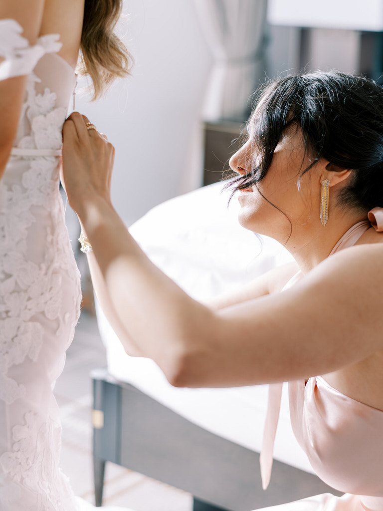 bride getting ready, bridesmaid zipping up wedding dress