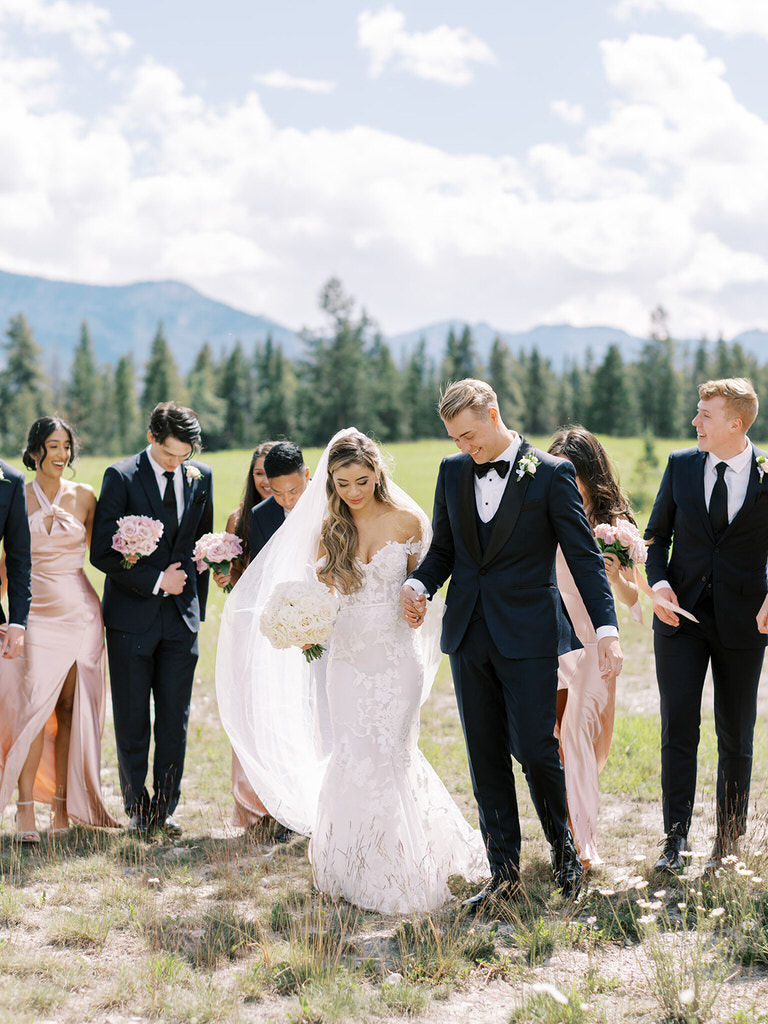 candid wedding party portraits in Canadian Rockies. Bride and Groom with groomsmen and bridesmaids. Pink satin dresses with pink and white roses. 