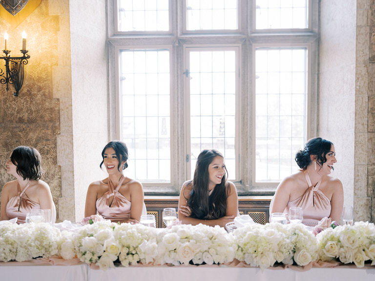 bridesmaids at head table giving a toast during wedding speeches, pink satin dresses, white roses