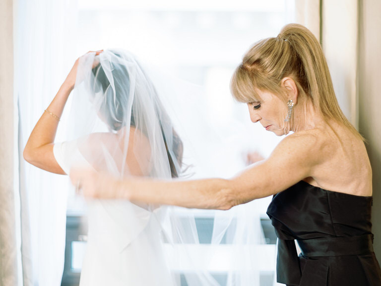 Mother of bride helps put on wedding veil Black wedding party colors, white off-shoulder dress