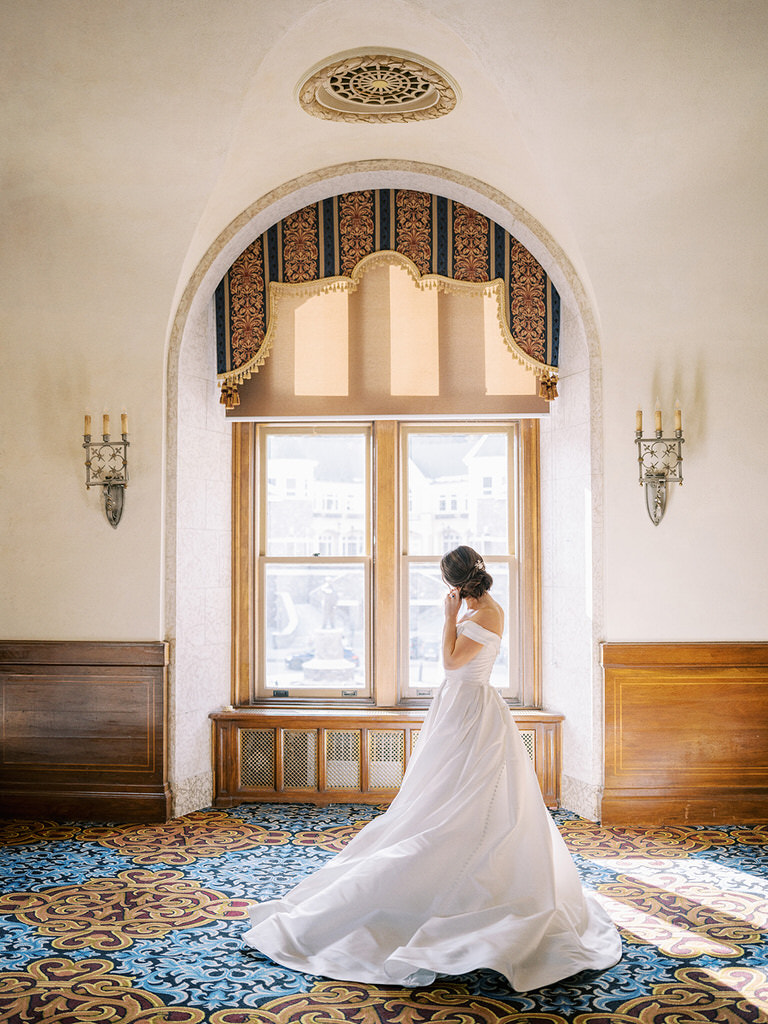 Mountain bride in wedding dress putting on earring at Banff Springs Hotel, Canada. 