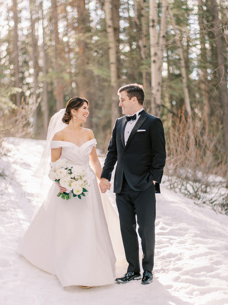 Mountain bride in strapless wedding dress with veil, couple portrait shot of bride and groom, holding hands full body, outside mountain photography  in Banff, Canada. 