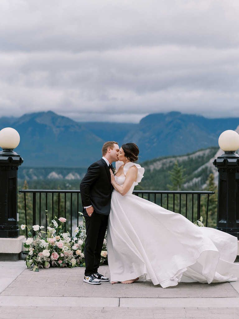 wedding couple portrait. Bride and groom kissing with mountain brackground. Groom in nike sneakers, bride barefoot. 