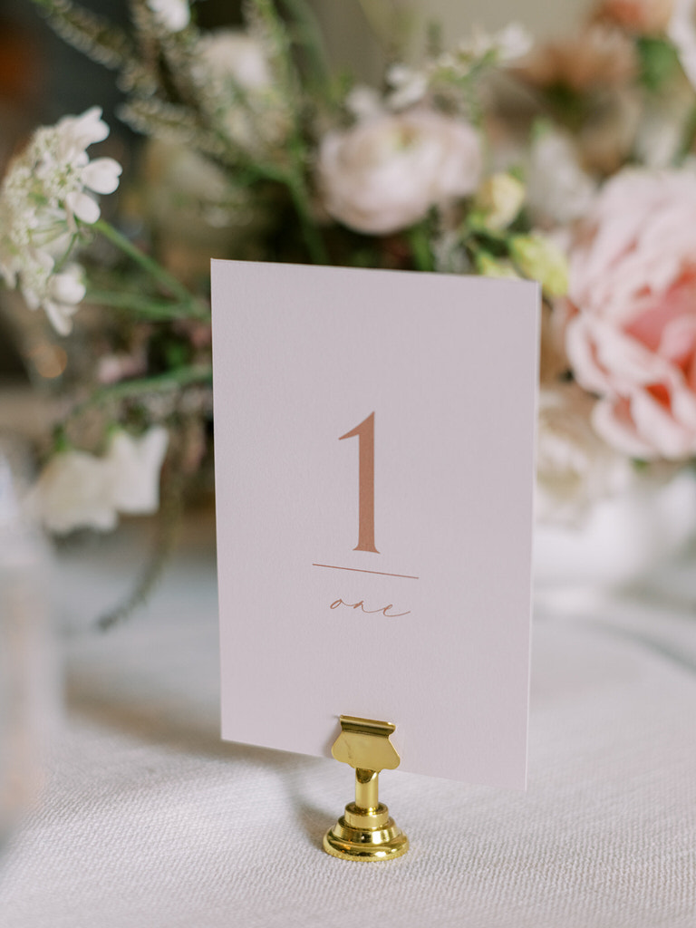 table marker for wedding reception space in Fairmont Banff Springs hotel. Light pink pastel and white florals, gold features, white linens. 