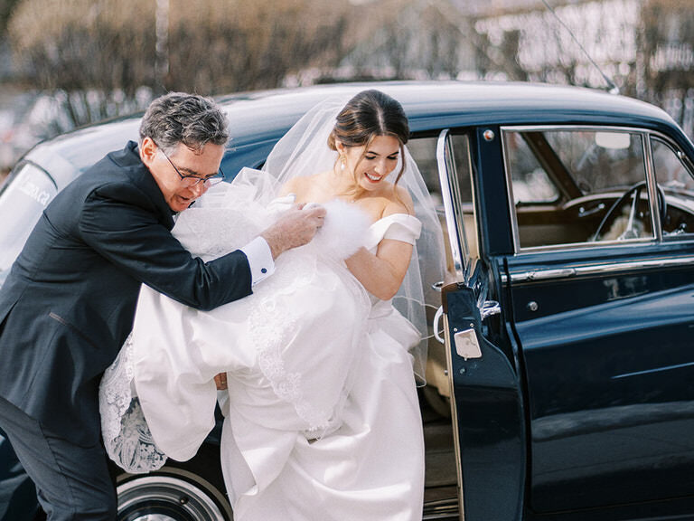 Mountain bride in strapless wedding dress, with veil exits car to wedding ceremony with father of bride in Banff, Canada. 