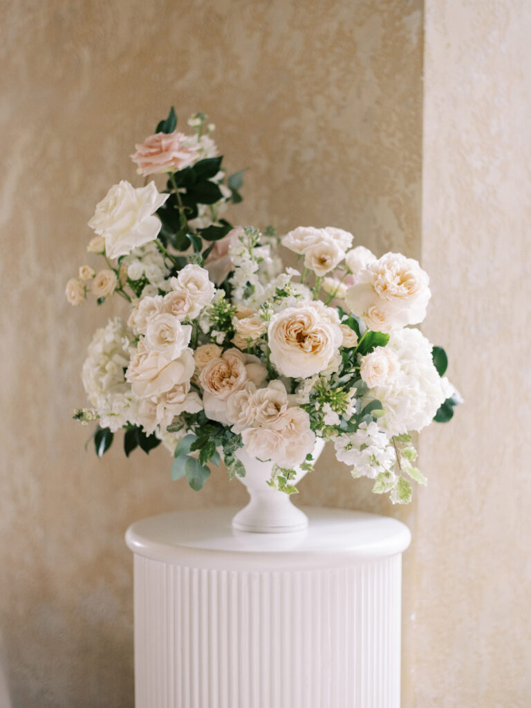 renaissance like floral arrangement with blush peach and white florals on a ribbed pillar captured by Banff Wedding Photographer Justine Milton
