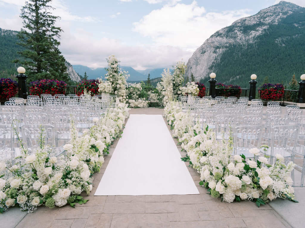 ceremony decor inspo with all white floral hedges lining the ceremony aisle on the Banff Springs Terrace captured by Banff Wedding Photographer Justine Milton